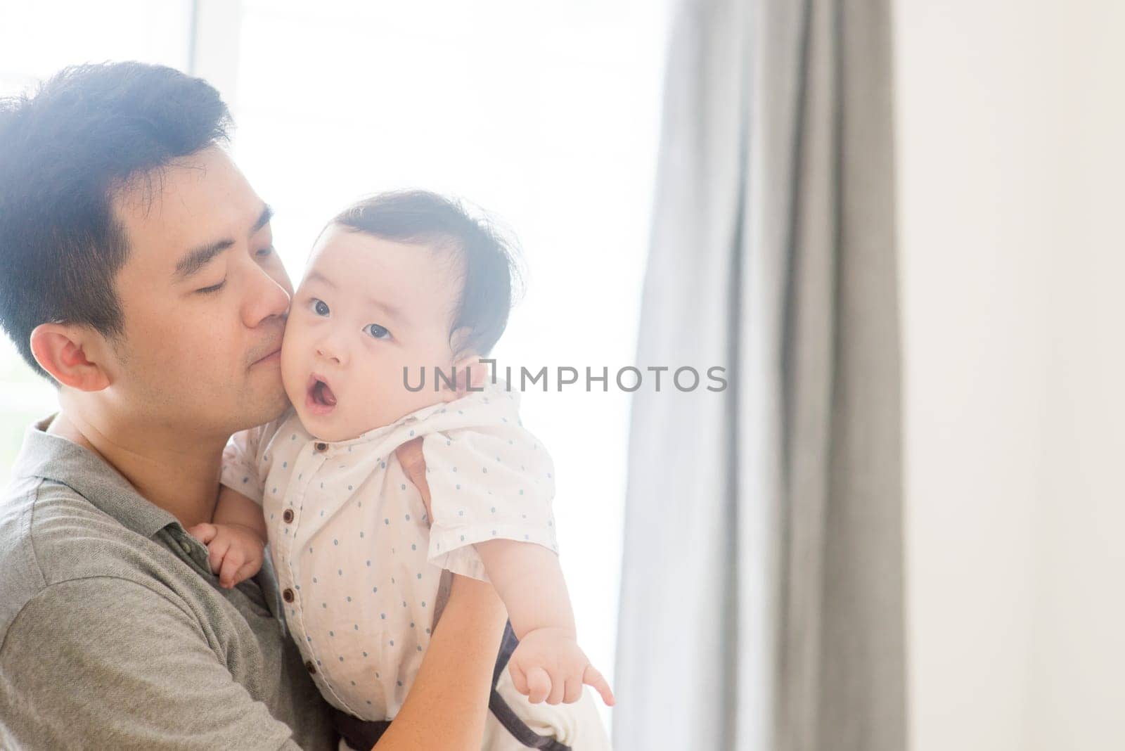 Happy Asian family at home. Father kissing son, living lifestyle indoors.