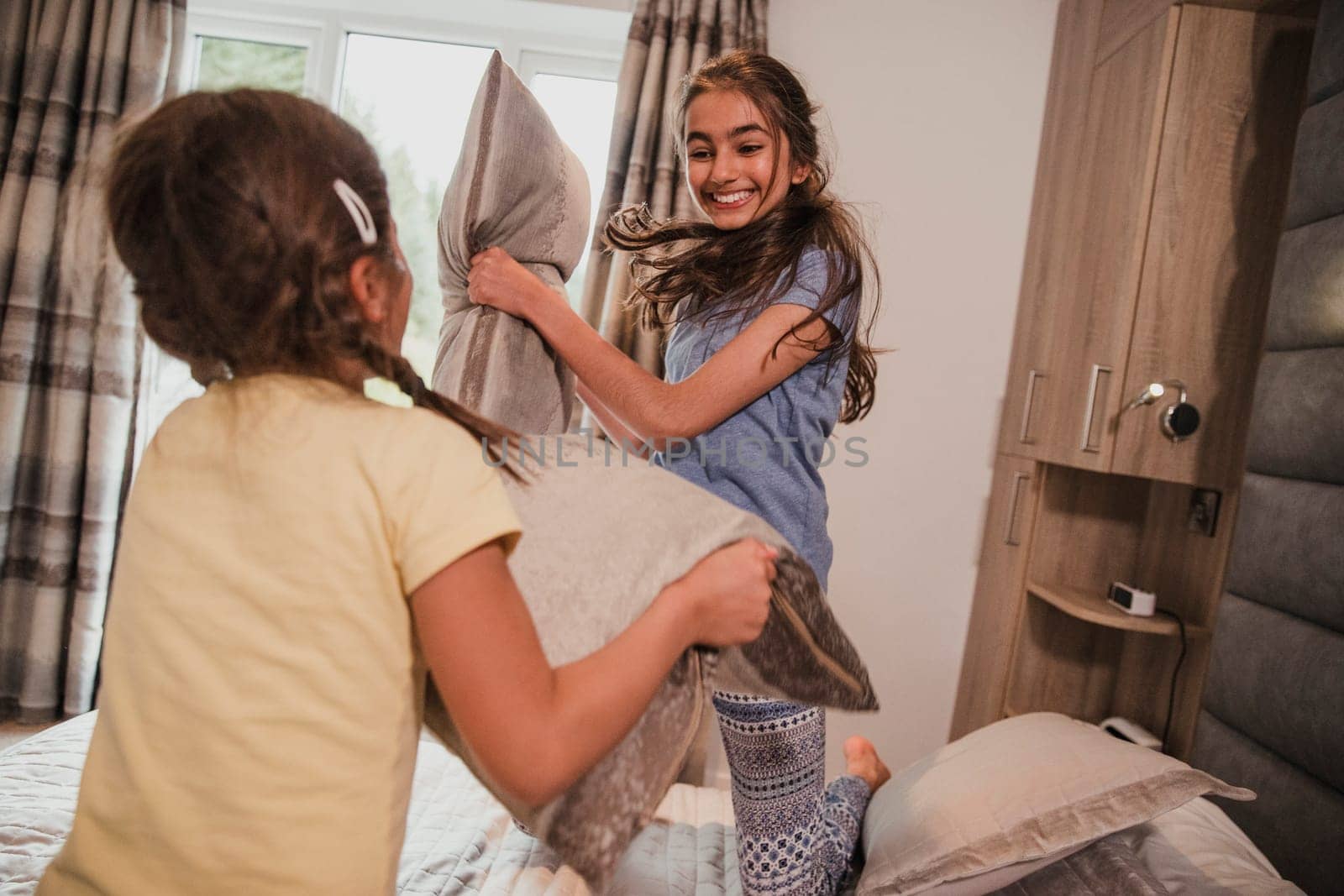 Two sisters are having a pillow fight in their room on holiday.