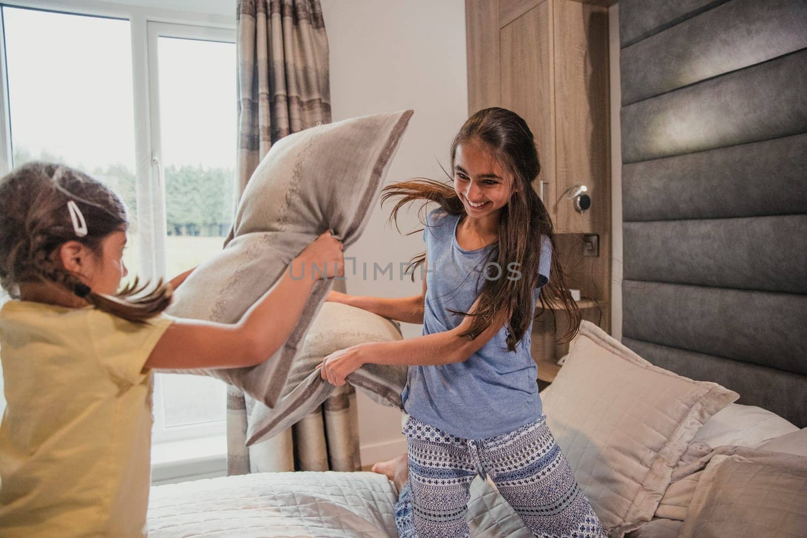 Two sisters are having a pillow fight in their room on holiday.