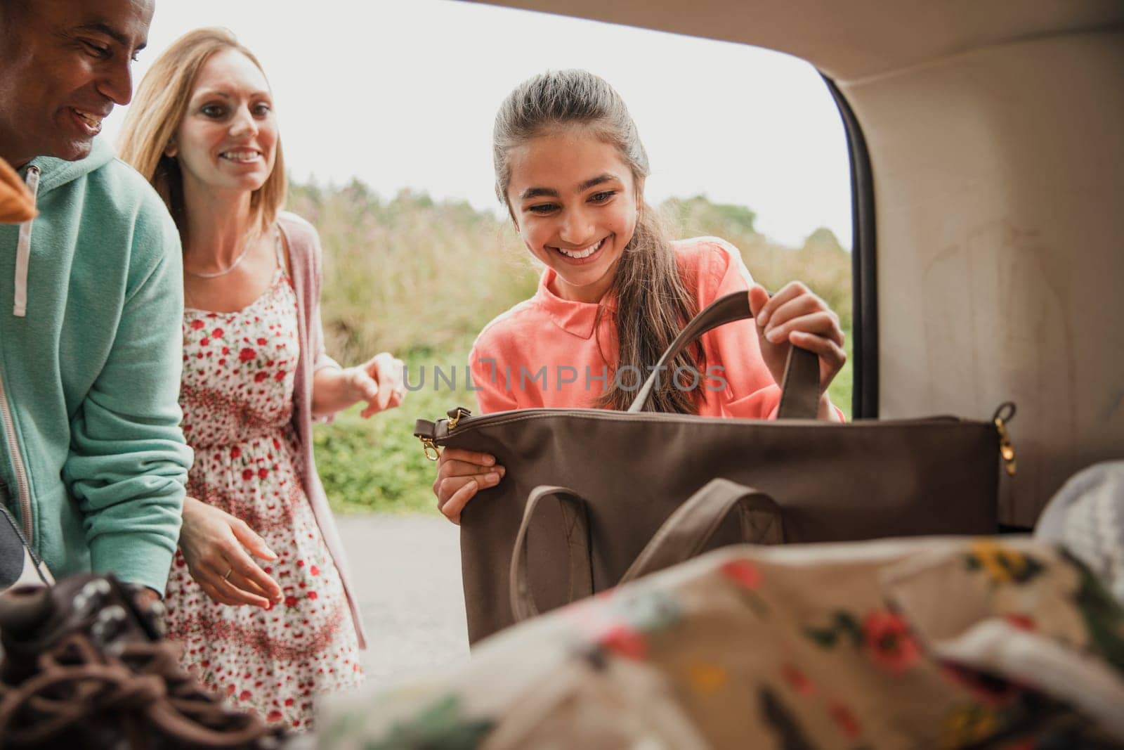 Female teenager helping unpack the car with her parents.