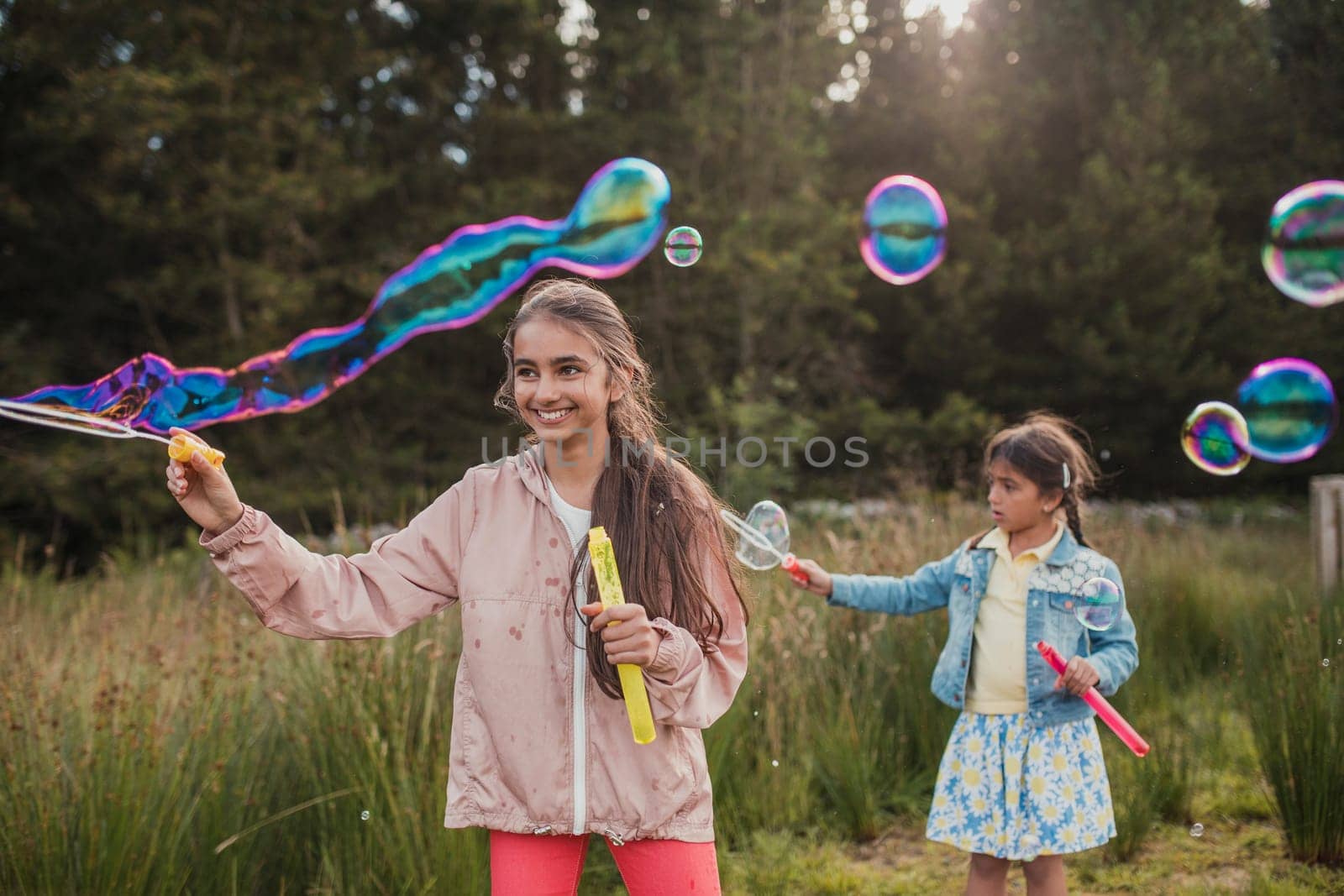 Two little girls creating bubbles in the woodlands on their holiday.