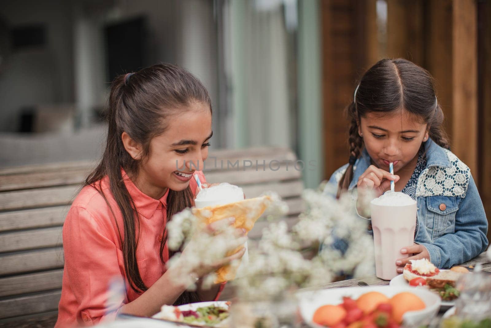 Two little girls enjoying milkshakes outside holiday cottage.