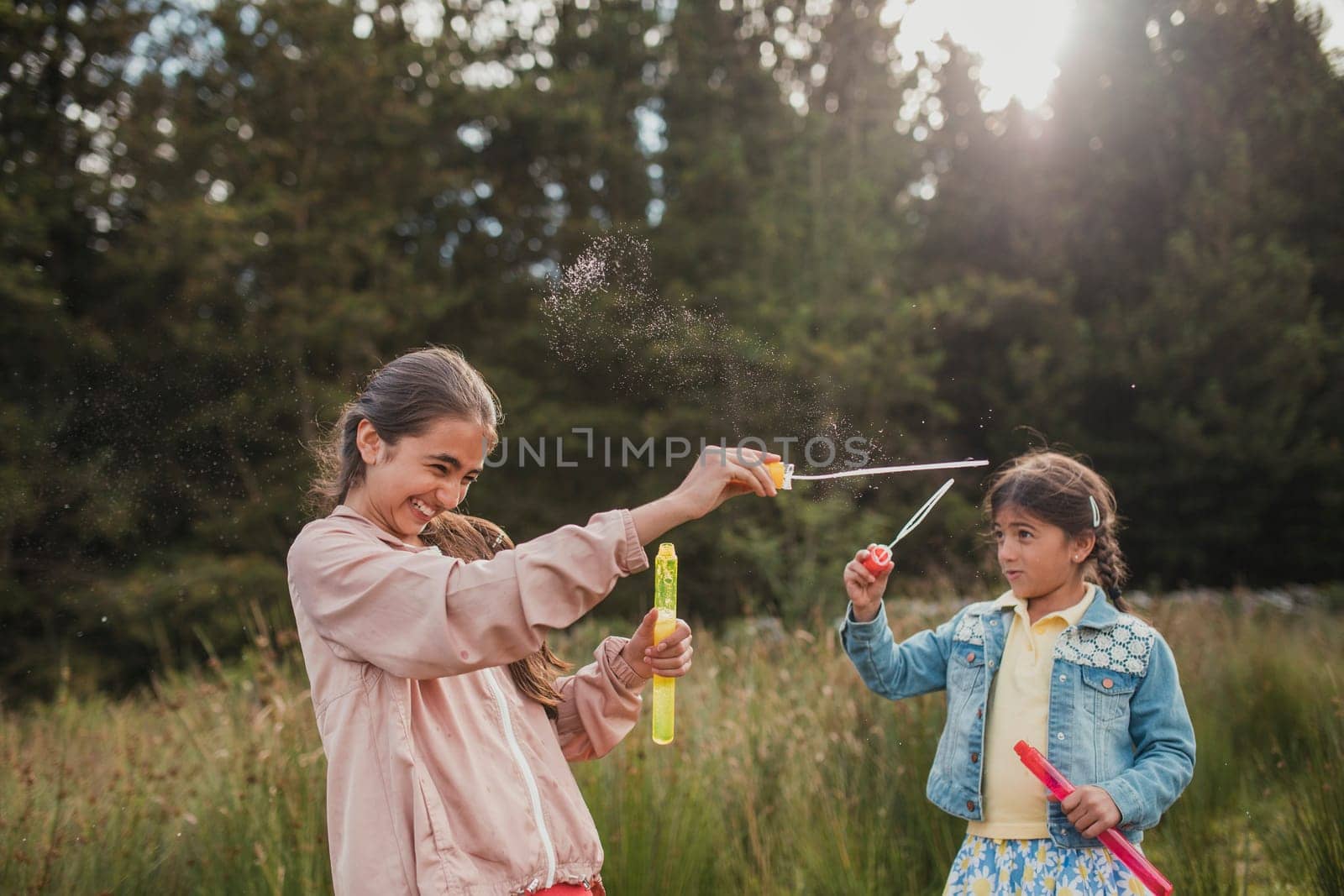 Two little girls creating bubbles in the woodlands on their holiday.