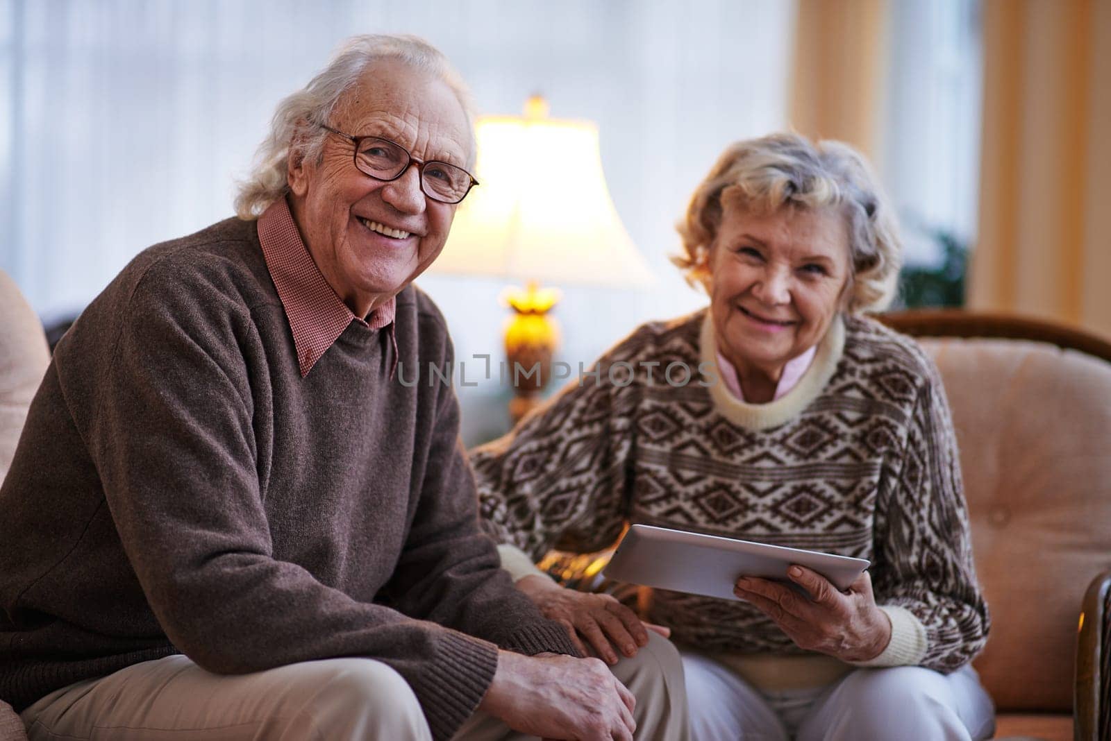 Smiling senior man looking at camera on background of his wife with touchpad