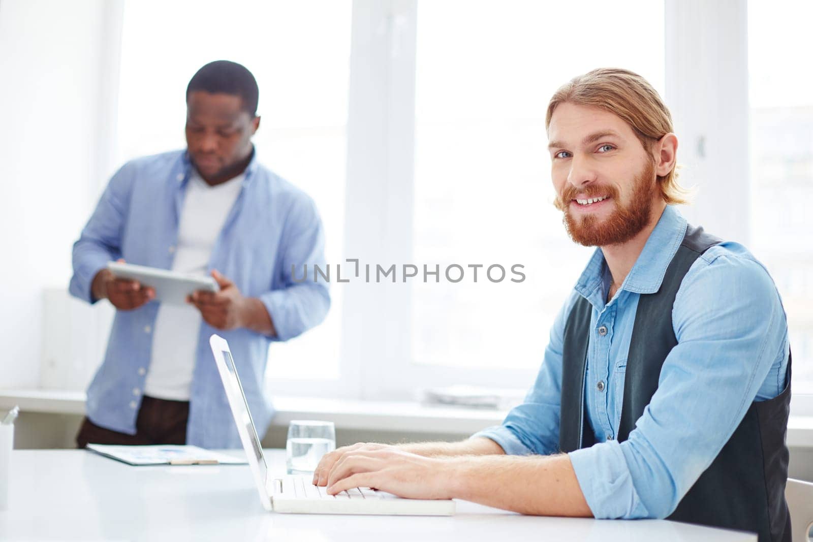 Successful manager computing at workplace with his colleague on background