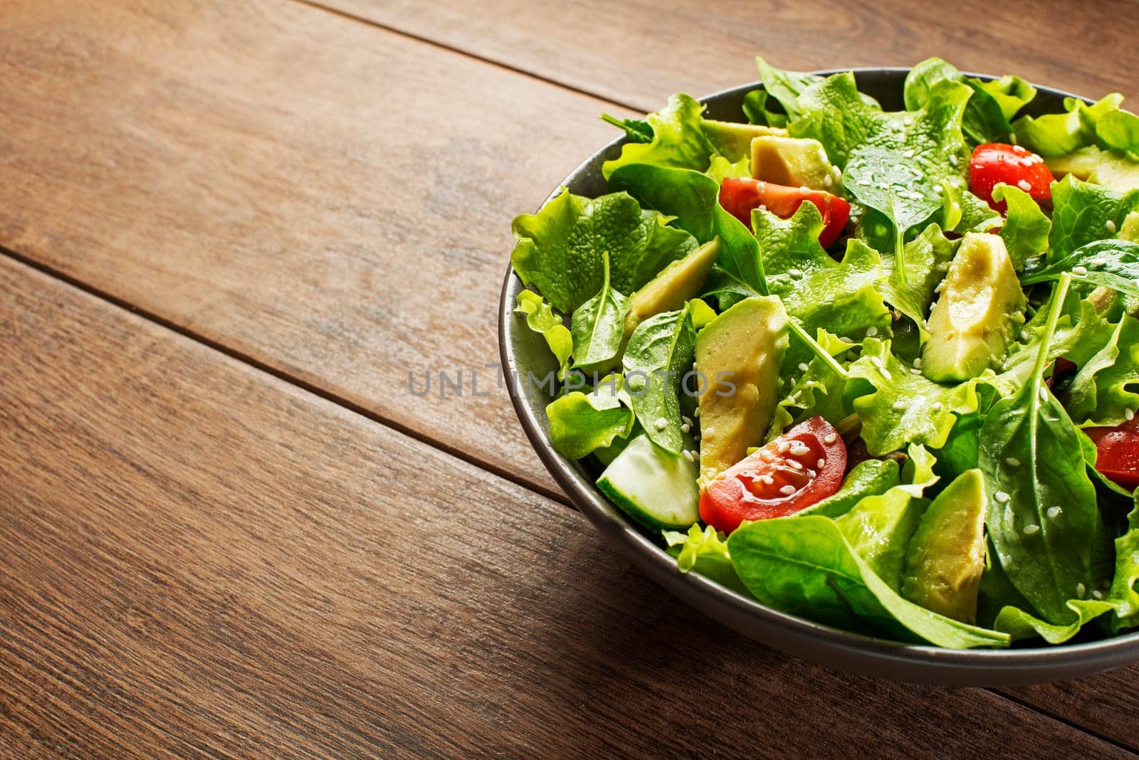 Green lettuce salad with avocado and fresh vegetables on wooden background.