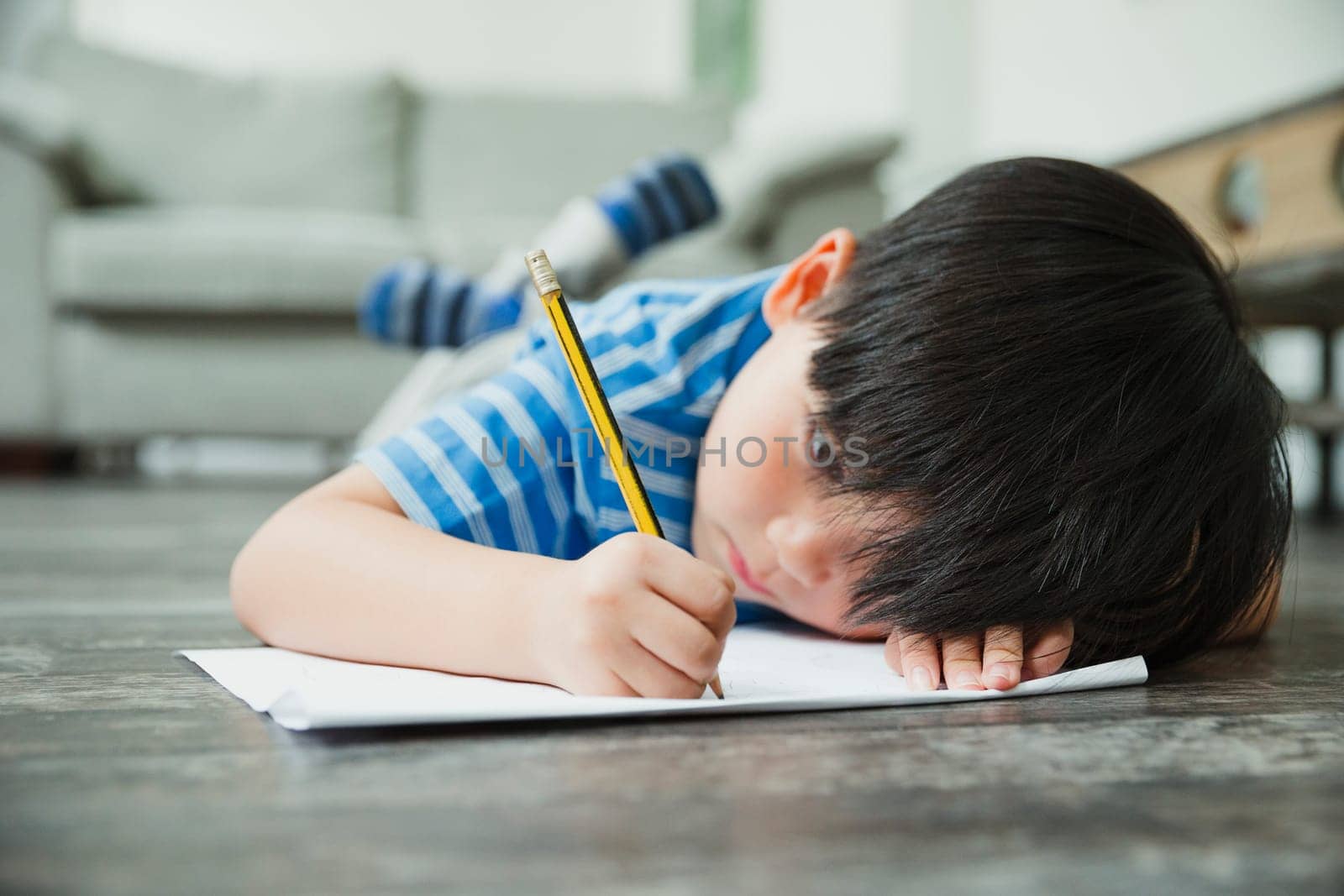 Little boy is lying on the floor, concentrating on his homework.