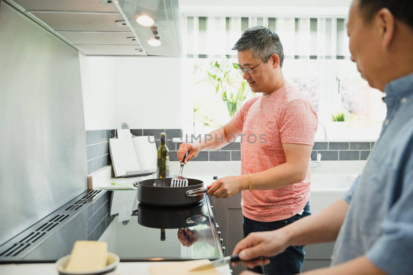 Mature man and his father are cooking a stir fry in the kitchen of their home.