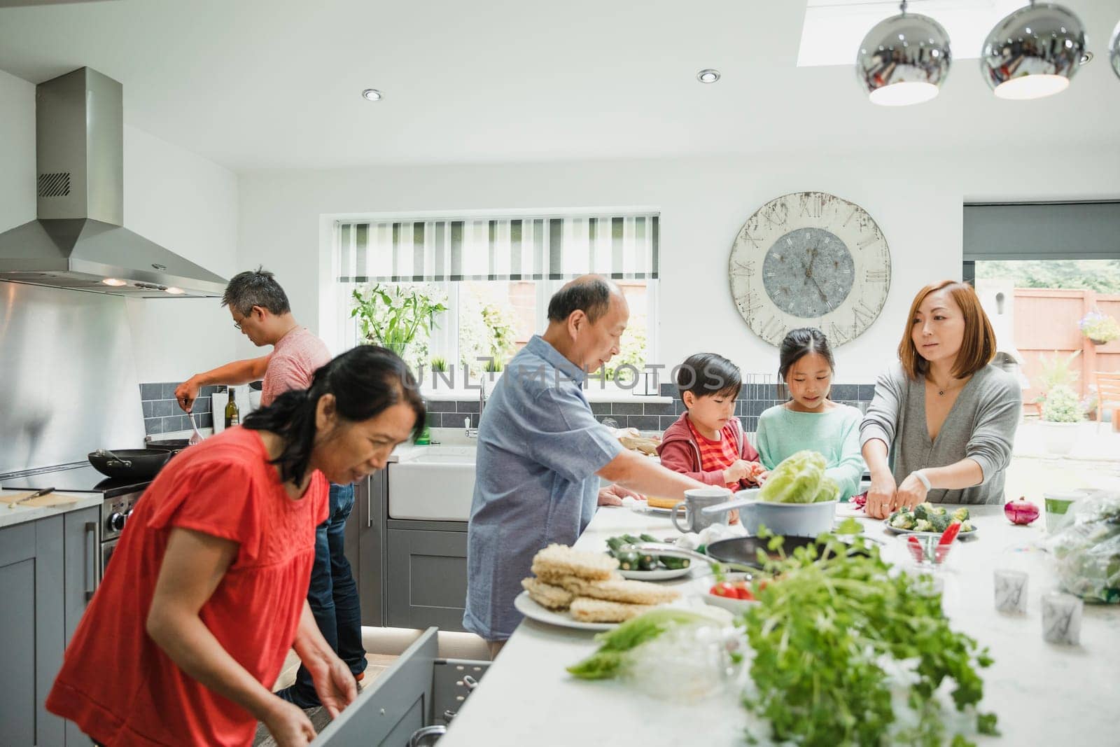 Three generation family are preparing vegetables for a stir fry in the kitchen of their home together.