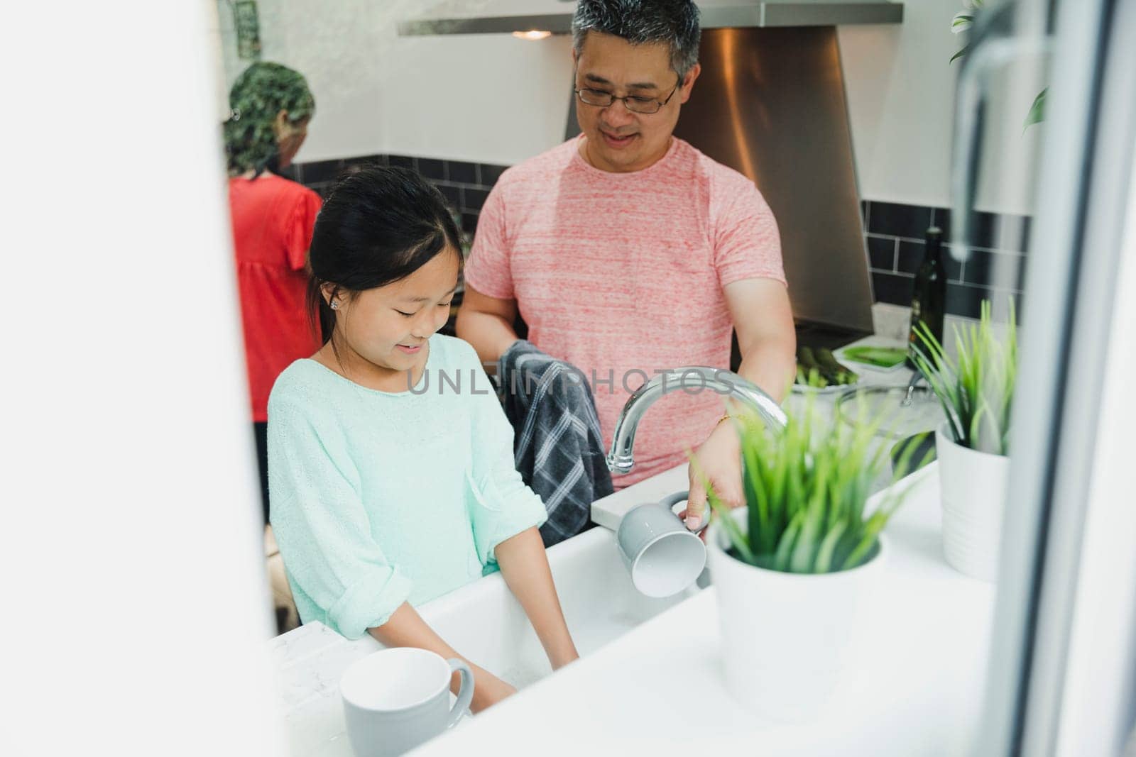Little girl is doing the chores in the kitchen with her father. She is washing the dishes and he is drying them.