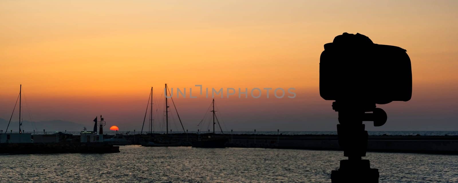 Camera on tripod with sea and sunset in background / Gouves, Crete, Greece