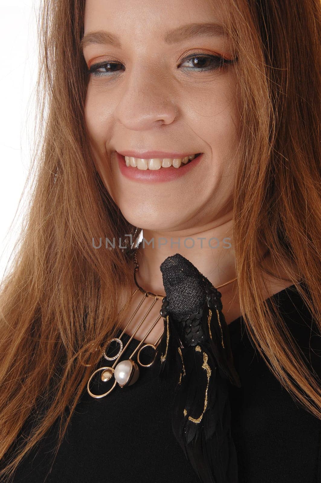 A beautiful young woman in a close up image with long brunette hair.having a fake black bird on her dress, isolated for white background.