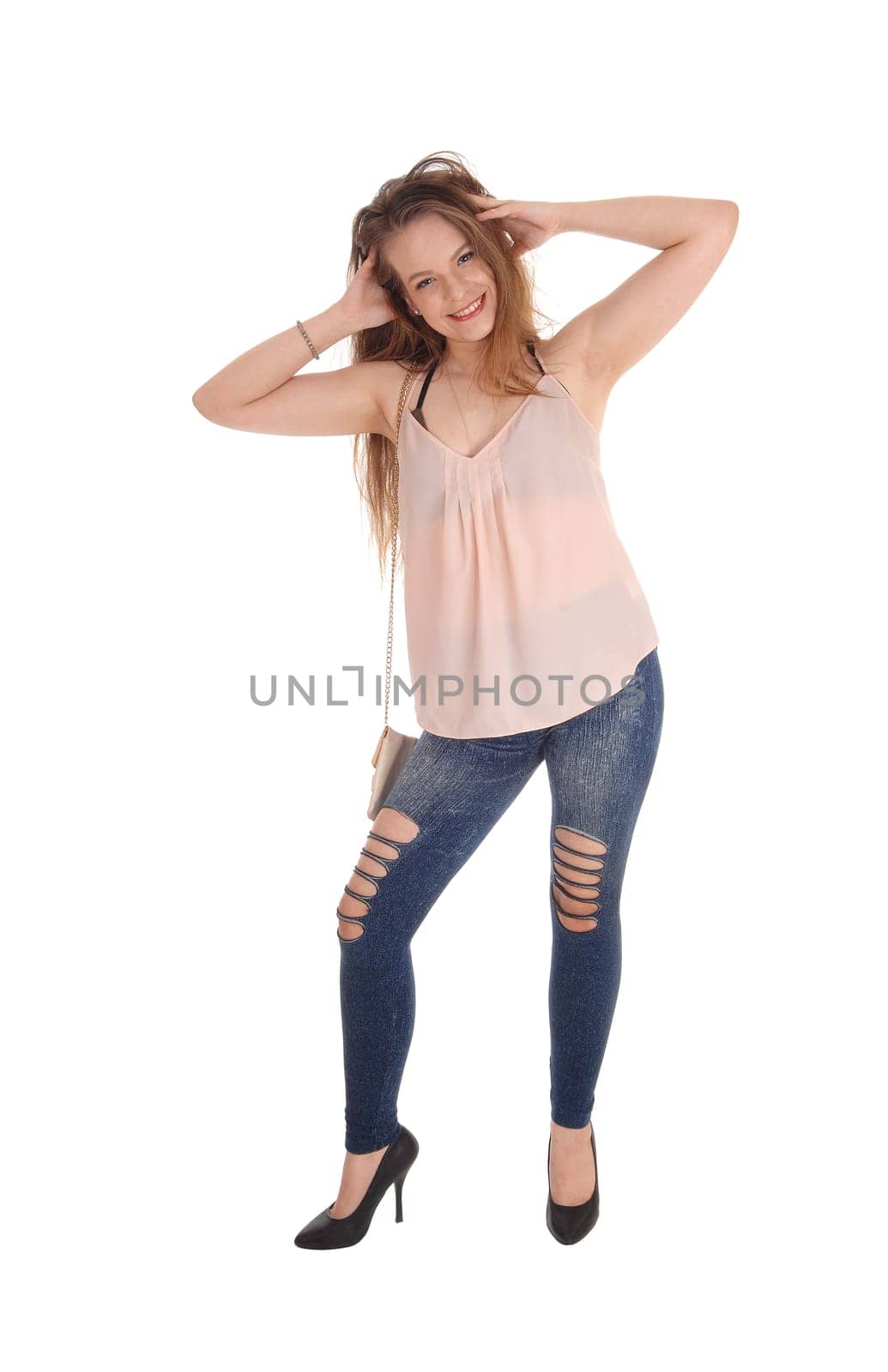A full body image of a beautiful young woman in jeans with her hands.in her hair, standing isolated for white background.