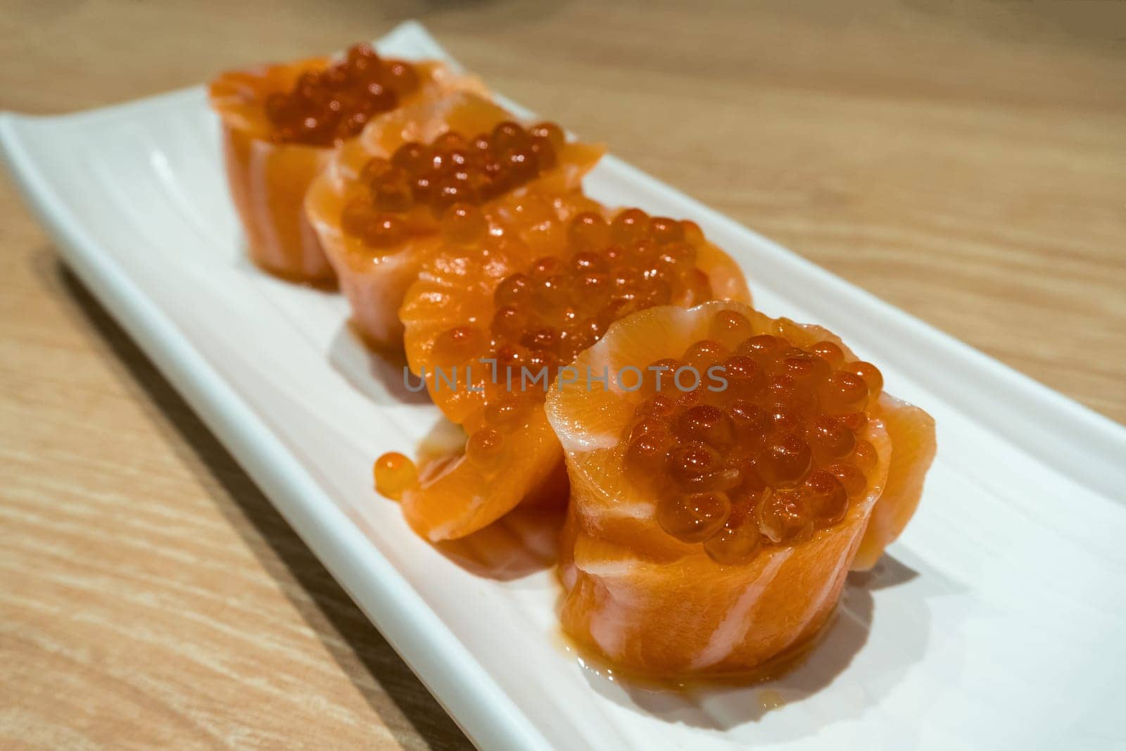Fresh Raw Salmon Sushi roll with fish egg roe on long white plate closeup macro