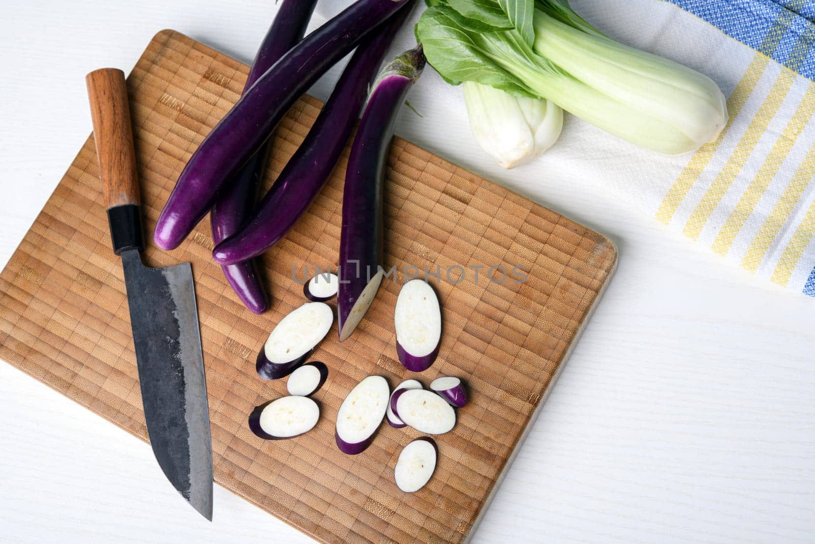 japanese eggplant on wooden board with cooking knife and pak choi salad