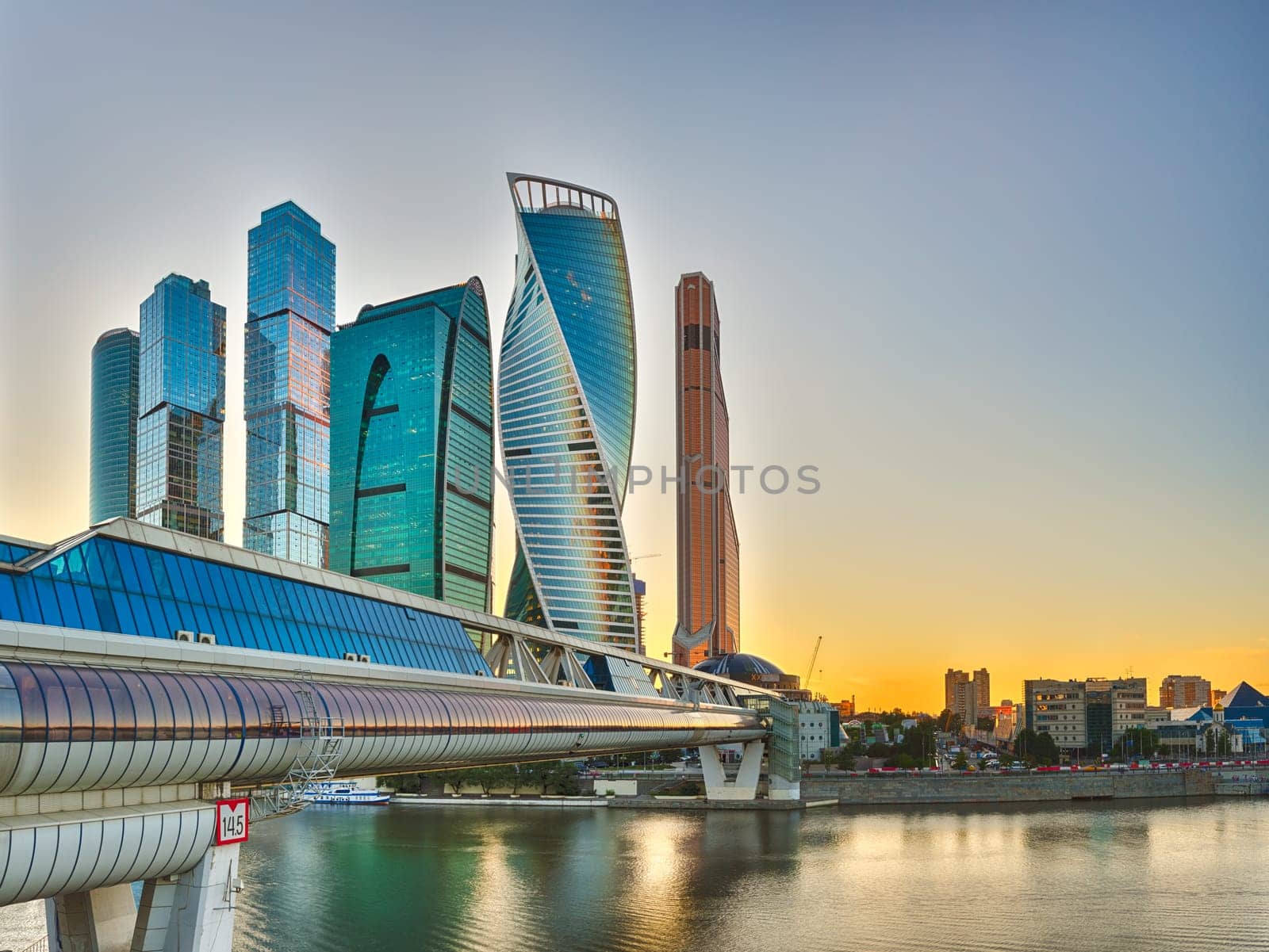 Moscow City at sunset. Moscow International Business Centre skyline at golden hour with Bagration Bridge and Moskva river in foreground