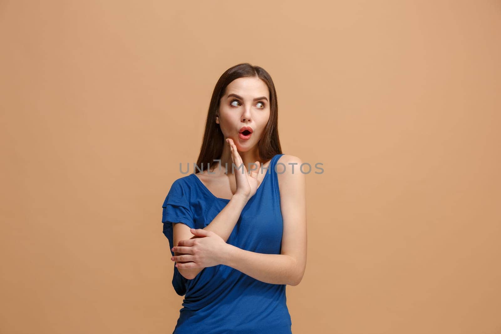 Wow. Beautiful female half-length portrait isolated on pastel studio backgroud. Young surprised woman holding hands by head, looking at camera. Human emotions, facial expression concept. Trendy colors