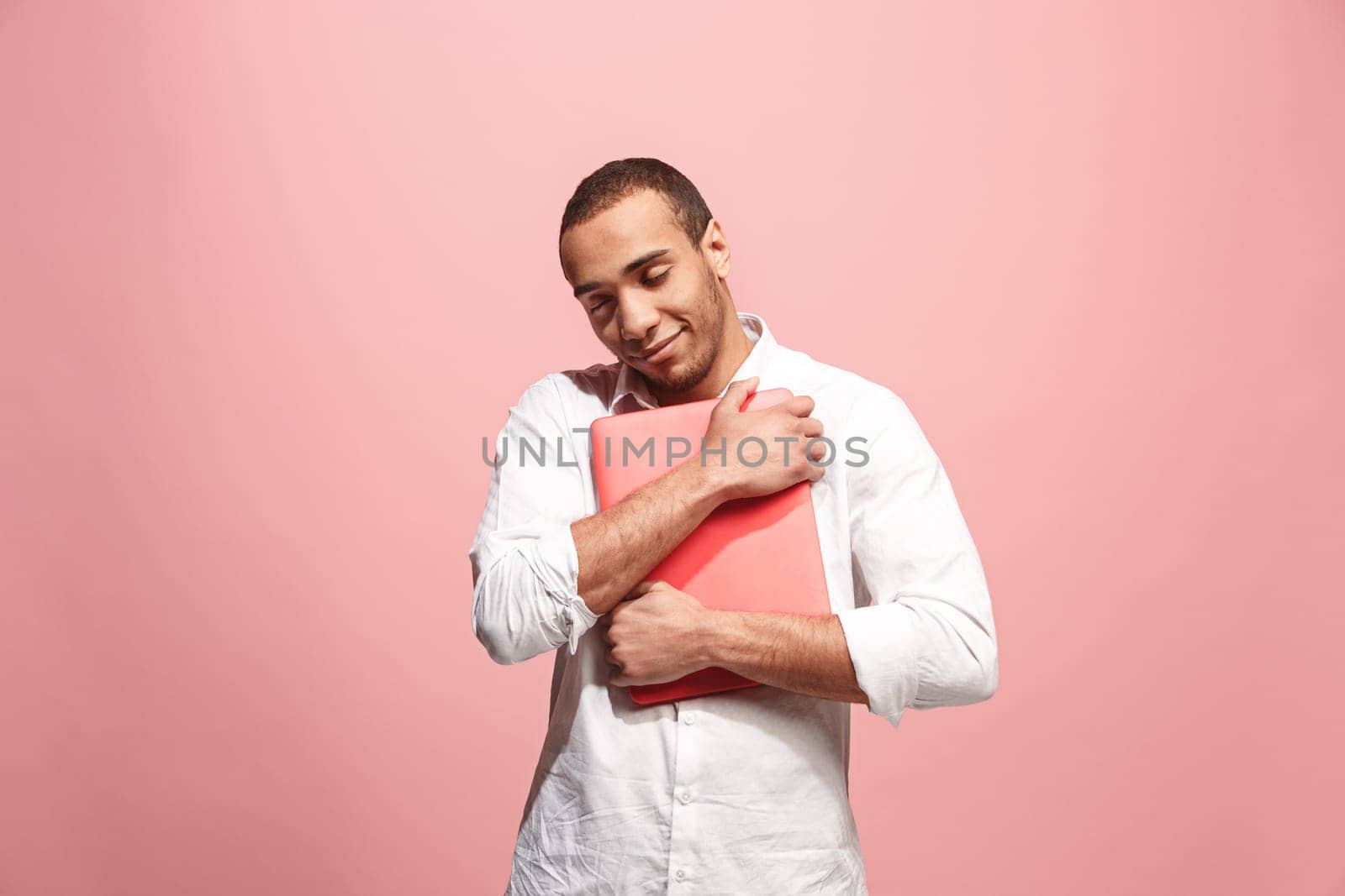 Afro businessman hugging laptop. Love to computer concept. Attractive male half-length front portrait, trendy pink studio backgroud. Young emotional bearded man. Human emotions, facial expression concept.