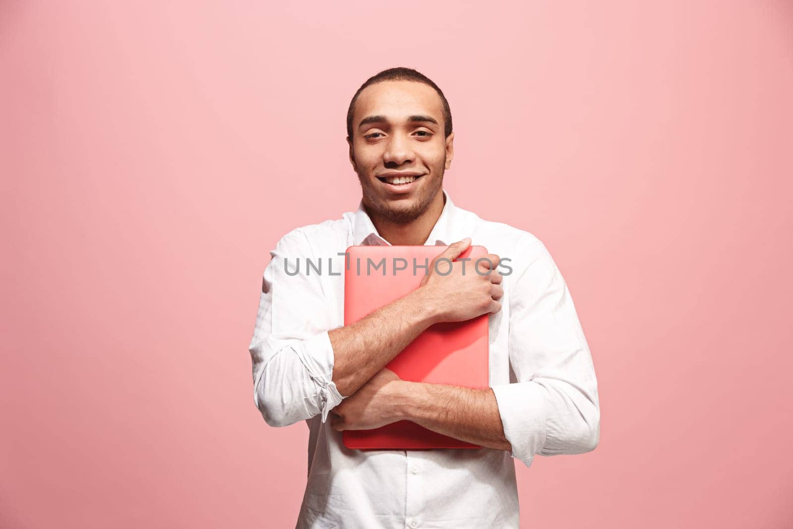 Afro businessman hugging laptop. Love to computer concept. Attractive male half-length front portrait, trendy pink studio backgroud. Young emotional bearded man. Human emotions, facial expression concept.