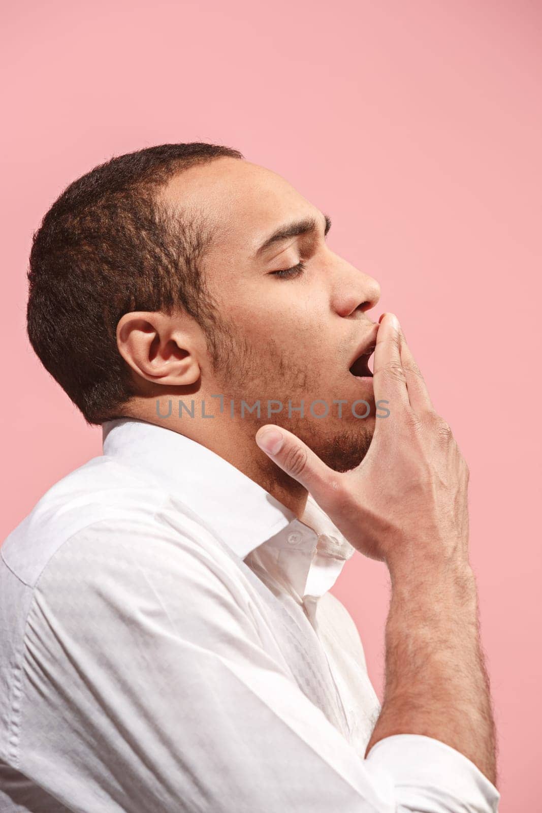 I am tired of everything. Bored man. Boring, dull, tedious concept. Young caucasian emotional afro man. Human emotions, facial expression concept. Studio isolated on trendy pink background. Profile