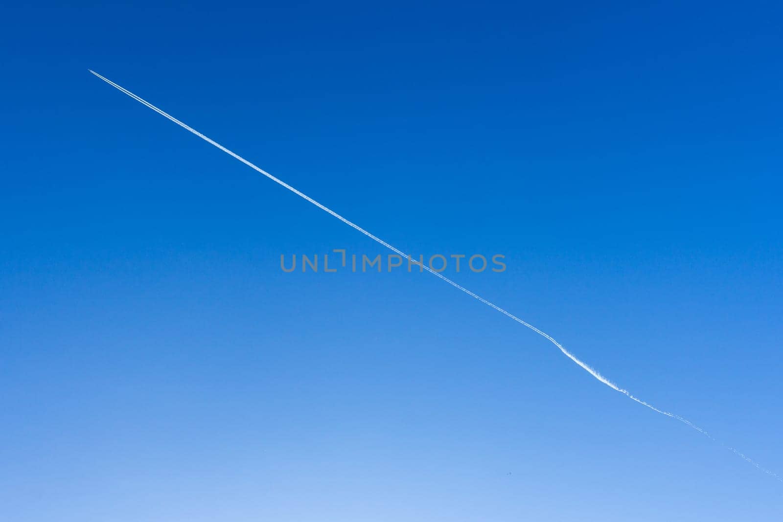 Airplane in the blue sky leaves white stripes behind him. The direction is diagonal. It can be used as a background. Space for text.
