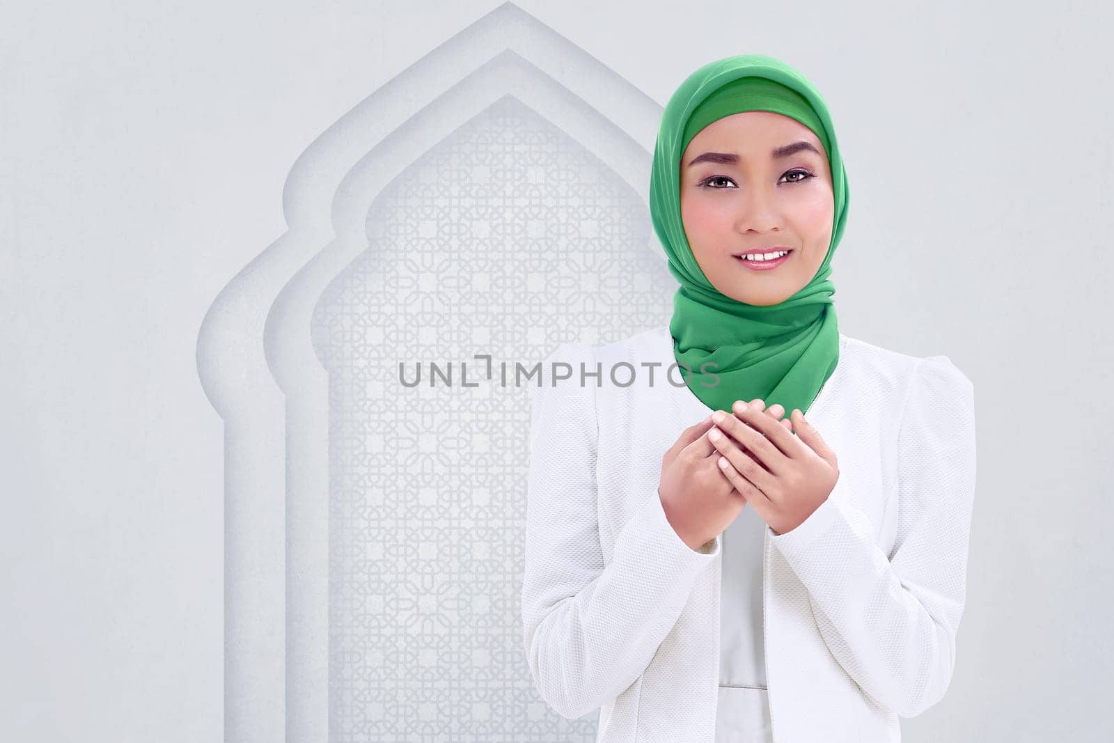 Smiling asian muslim woman raising hand and pray with white wall background