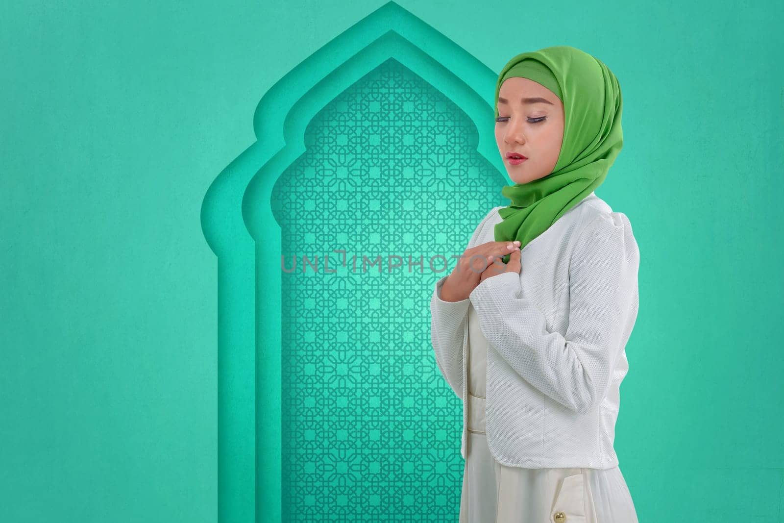 Pretty asian muslim woman with traditional dress praying against green wall background