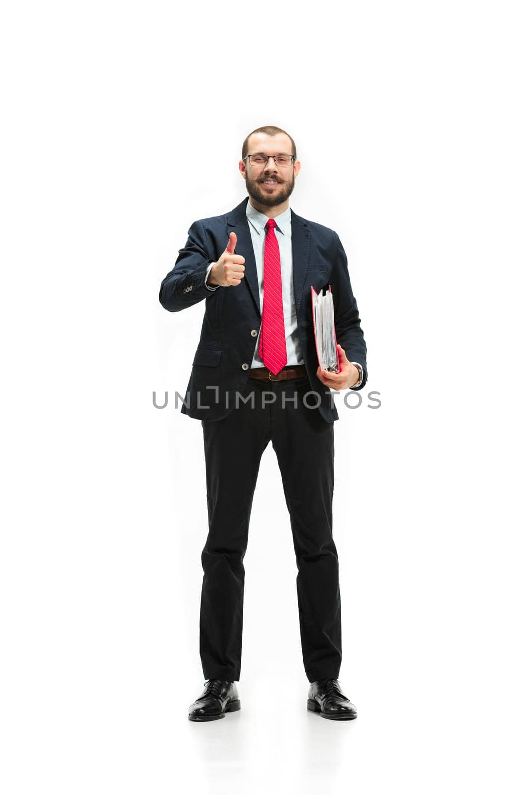 Full body or full-length portrait of businessman with red folder on white studio background. Serious bearded young man in glasses, suit, red tie standing in office. Business, career, success concept.