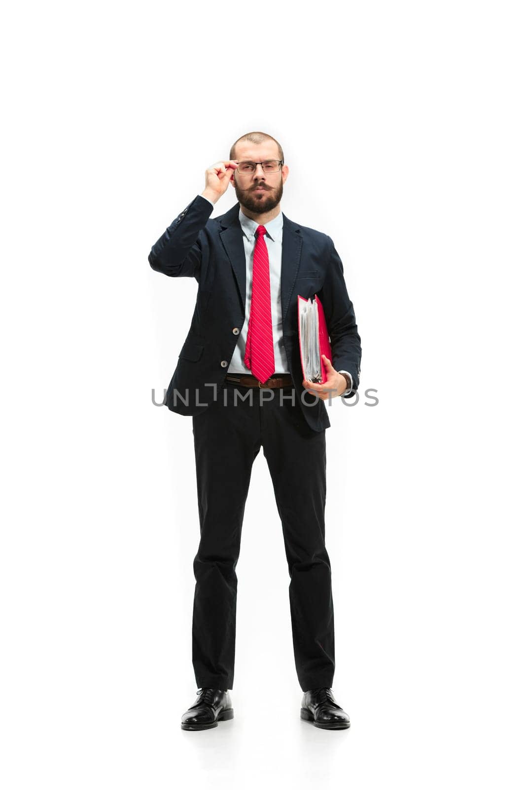 Full body or full-length portrait of businessman with red folder on white studio background. Serious bearded young man in glasses, suit, red tie standing in office. Business, career, success concept.