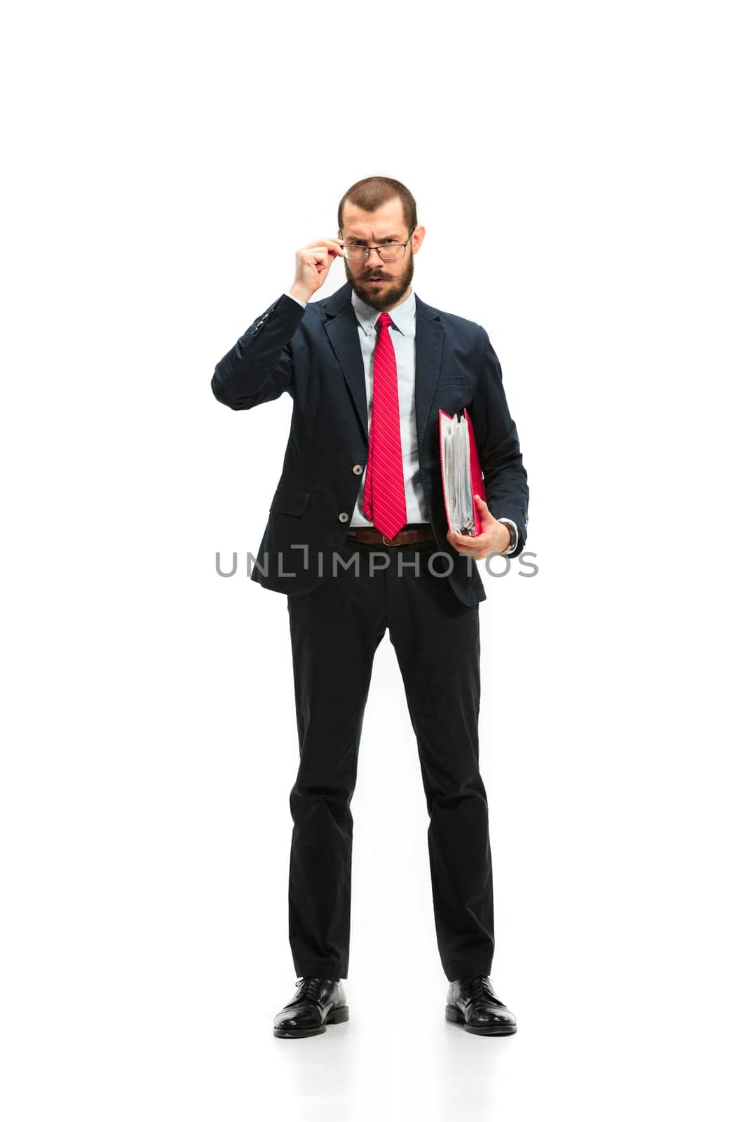 Full body or full-length portrait of businessman with red folder on white studio background. Serious bearded young man in glasses, suit, red tie standing in office. Business, career, success concept.