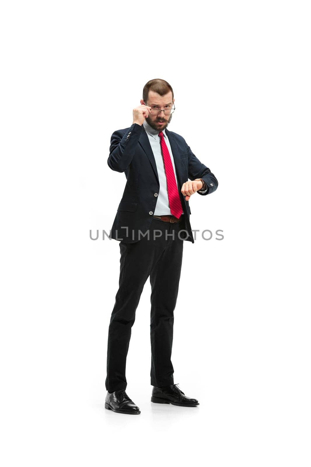 Businessman looking at his watch on his hand, watching the time. portrait of businessman on white studio background. Serious bearded young man in glasses, suit, red tie standing in office. Business concept.
