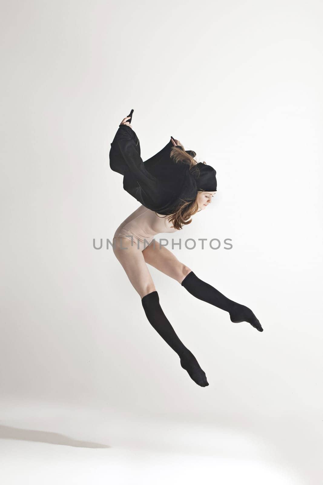 Young beautiful dancer in beige swimsuit dancing on gray studio background. Front view. Young female classical ballet dancer. Ballerina project. Modern choreography, contemporary. Fit caucasian moman