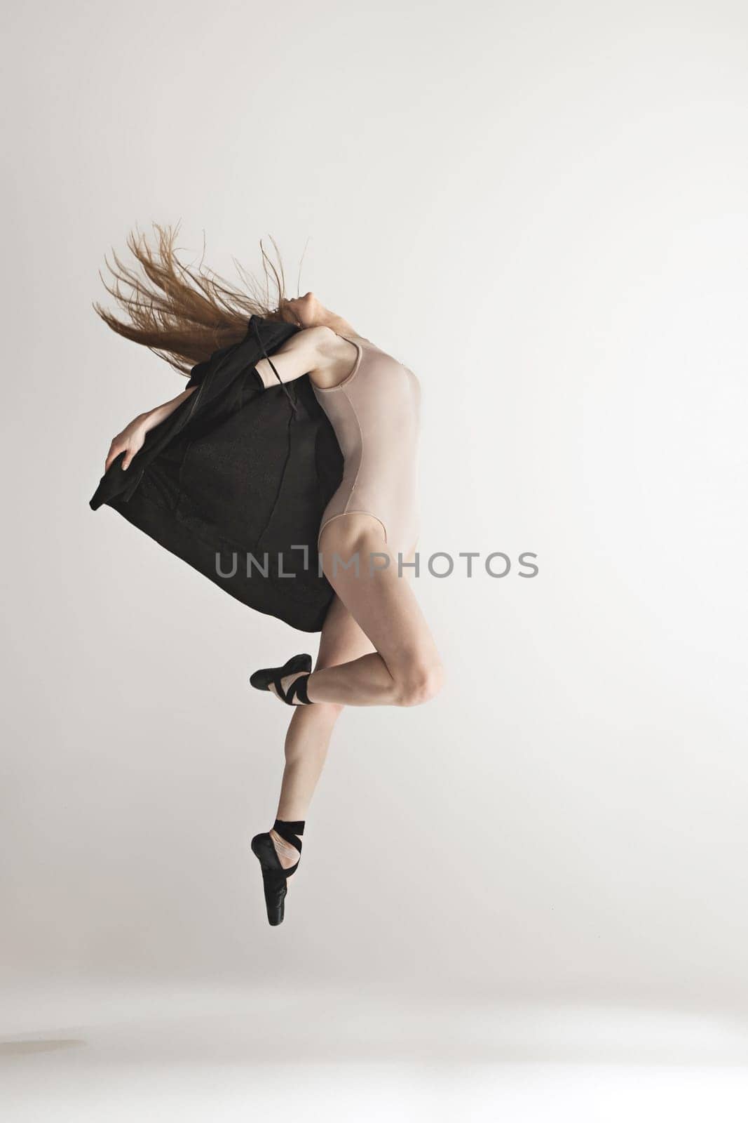 Young beautiful dancer in beige swimsuit dancing on gray studio background. Front view. Young female classical ballet dancer. Ballerina project. Modern choreography, contemporary. Fit caucasian moman