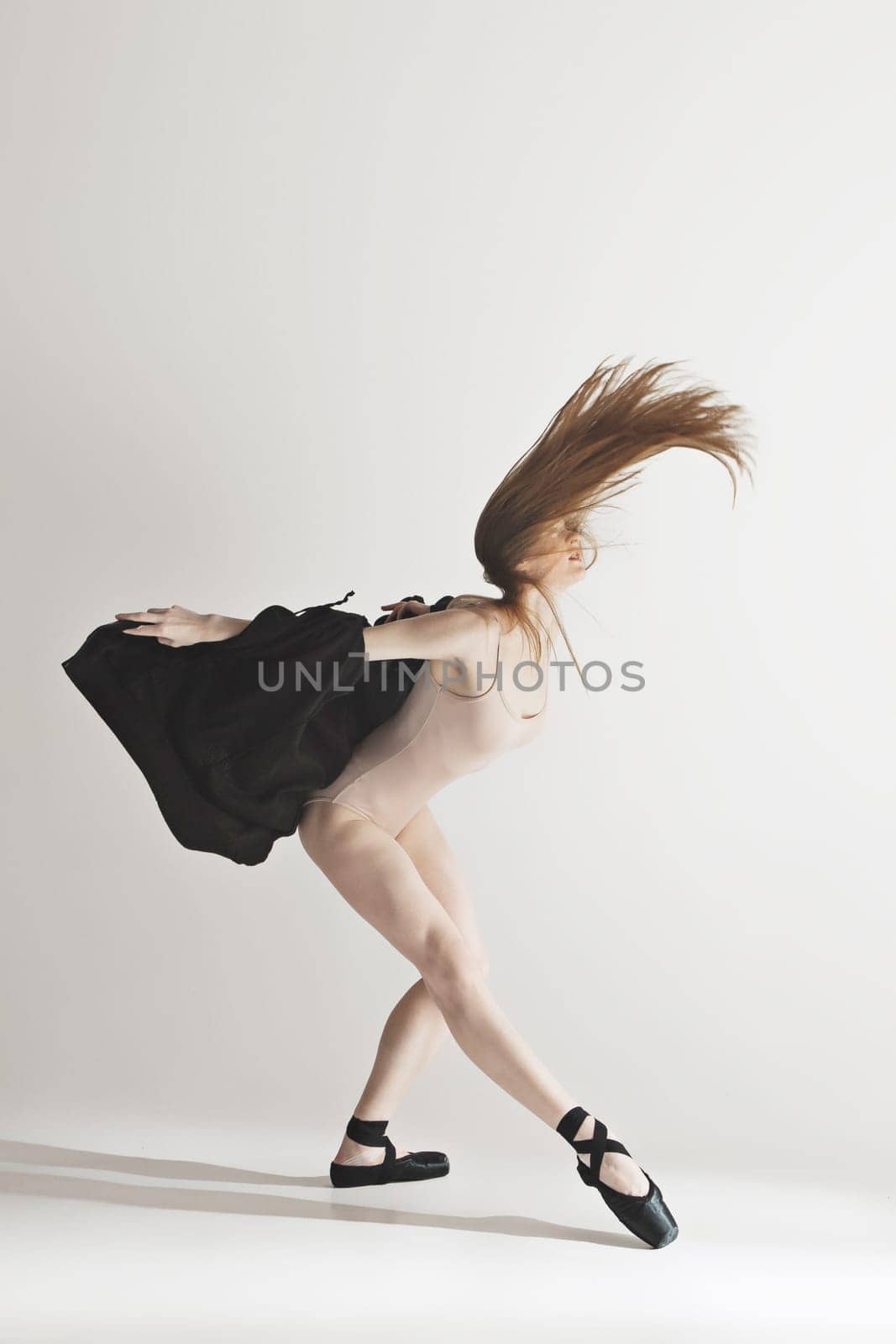 Young beautiful dancer in beige swimsuit dancing on gray studio background. Front view. Young female classical ballet dancer. Ballerina project. Modern choreography, contemporary. Fit caucasian moman