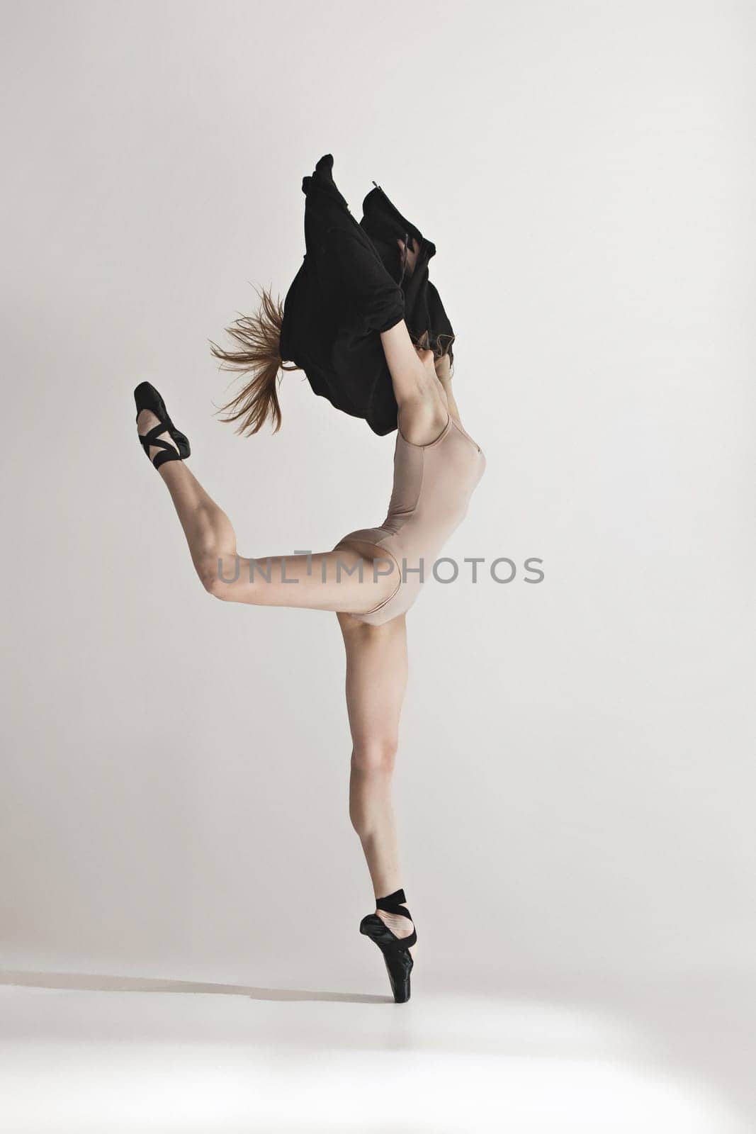 Young beautiful dancer in beige swimsuit dancing on gray studio background. Front view. Young female classical ballet dancer. Ballerina project. Modern choreography, contemporary. Fit caucasian moman