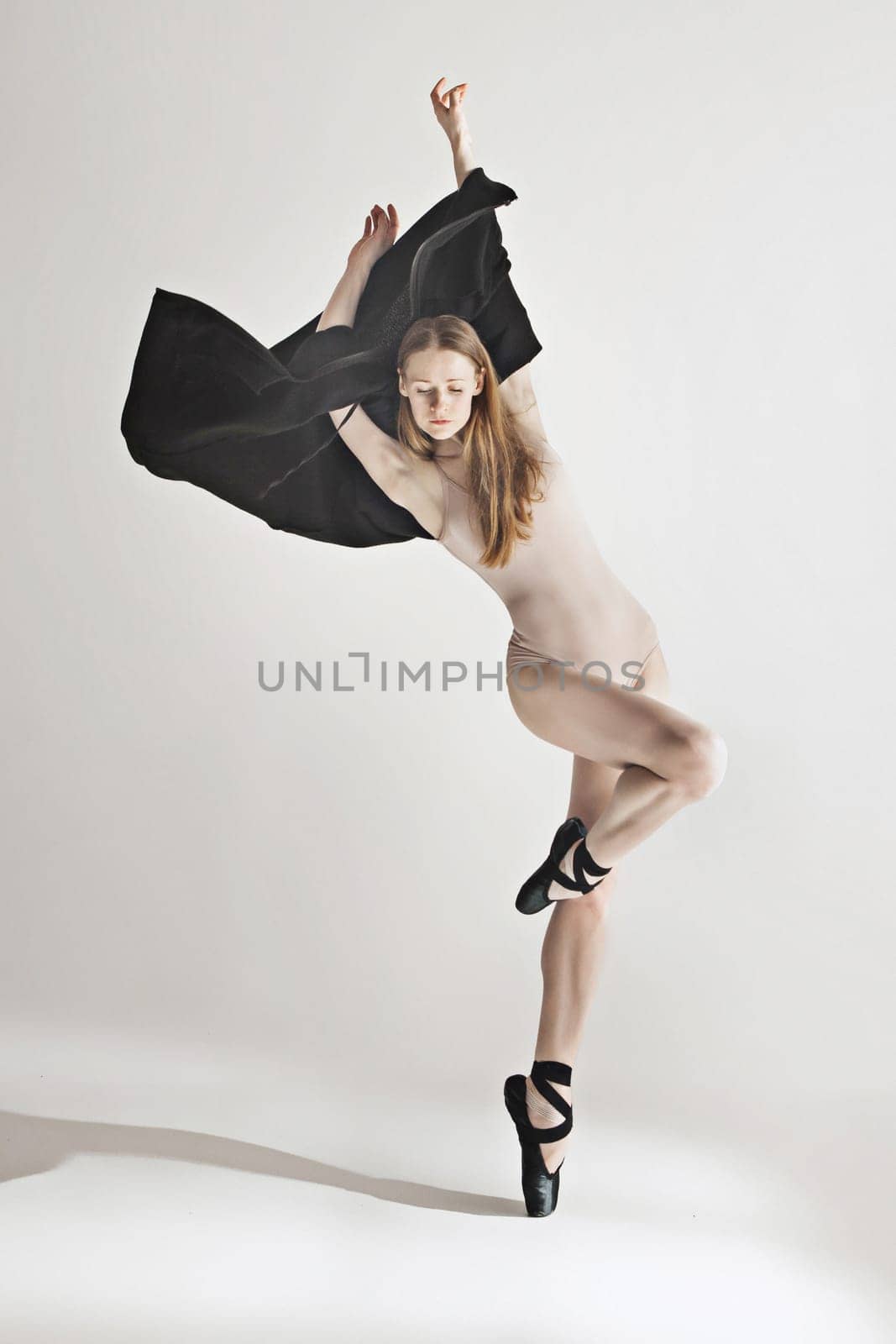 Young beautiful dancer in beige swimsuit dancing on gray studio background. Front view. Young female classical ballet dancer. Ballerina project. Modern choreography, contemporary. Fit caucasian moman