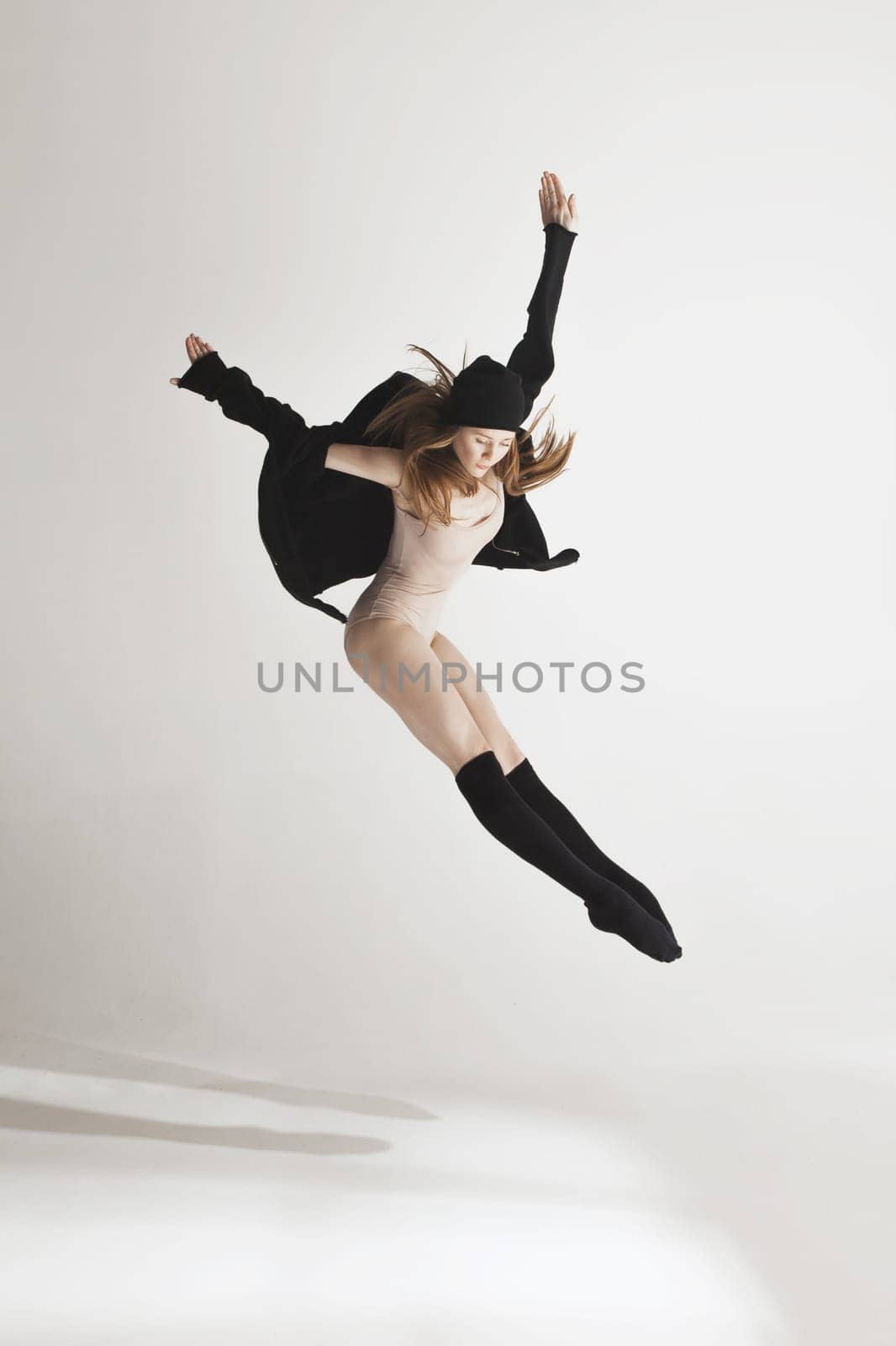 Young beautiful dancer in beige swimsuit dancing on gray studio background. Front view. Young female classical ballet dancer. Ballerina project. Modern choreography, contemporary. Fit caucasian moman