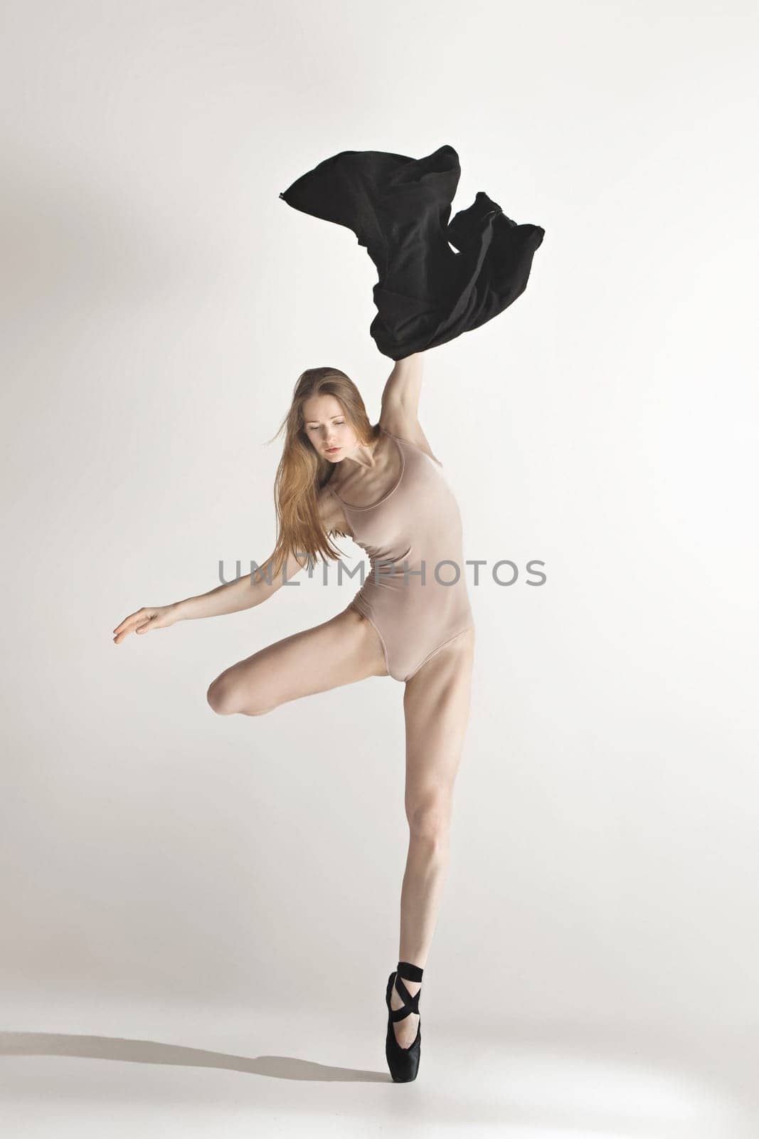 Young beautiful dancer in beige swimsuit dancing on gray studio background. Front view. Young female classical ballet dancer. Ballerina project. Modern choreography, contemporary. Fit caucasian moman