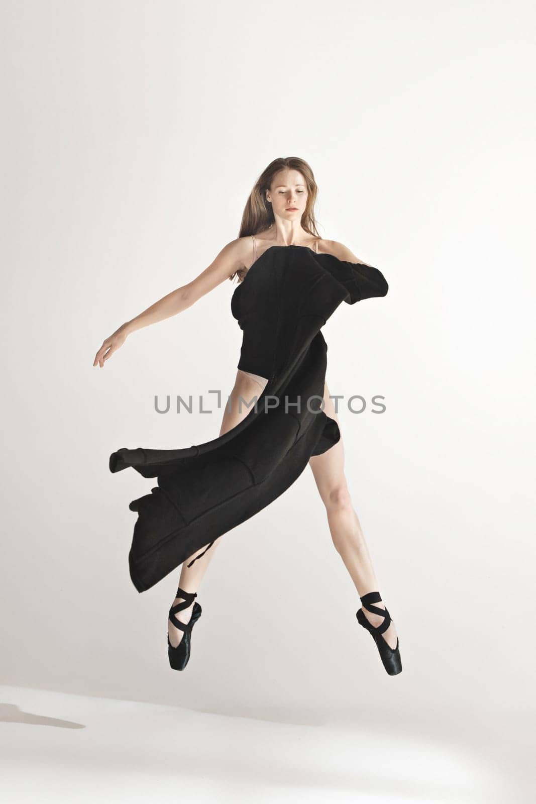 Young beautiful dancer in beige swimsuit dancing on gray studio background. Front view. Young female classical ballet dancer. Ballerina project. Modern choreography, contemporary. Fit caucasian moman