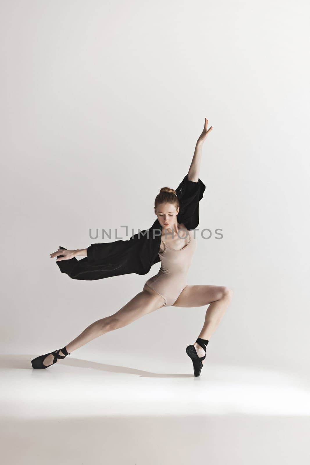 Young beautiful dancer in beige swimsuit dancing on gray studio background. Front view. Young female classical ballet dancer. Ballerina project. Modern choreography, contemporary. Fit caucasian moman