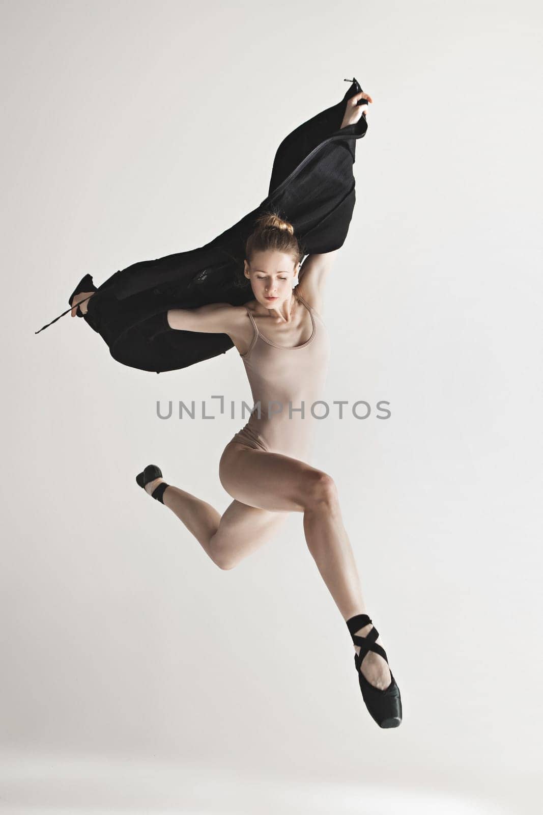 Young beautiful dancer in beige swimsuit dancing on gray studio background. Front view. Young female classical ballet dancer. Ballerina project. Modern choreography, contemporary. Fit caucasian moman