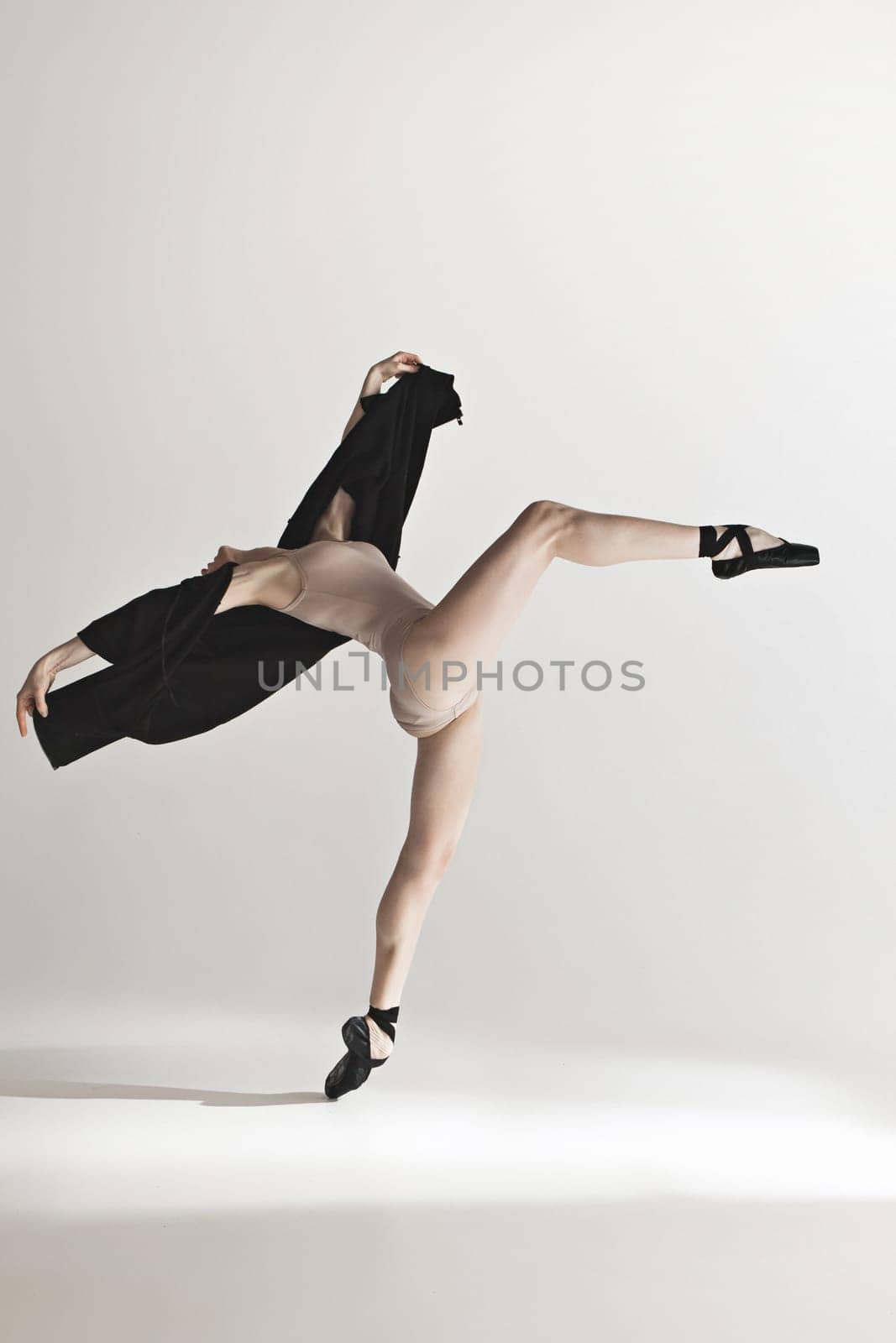 Young beautiful dancer in beige swimsuit dancing on gray studio background. Front view. Young female classical ballet dancer. Ballerina project. Modern choreography, contemporary. Fit caucasian moman