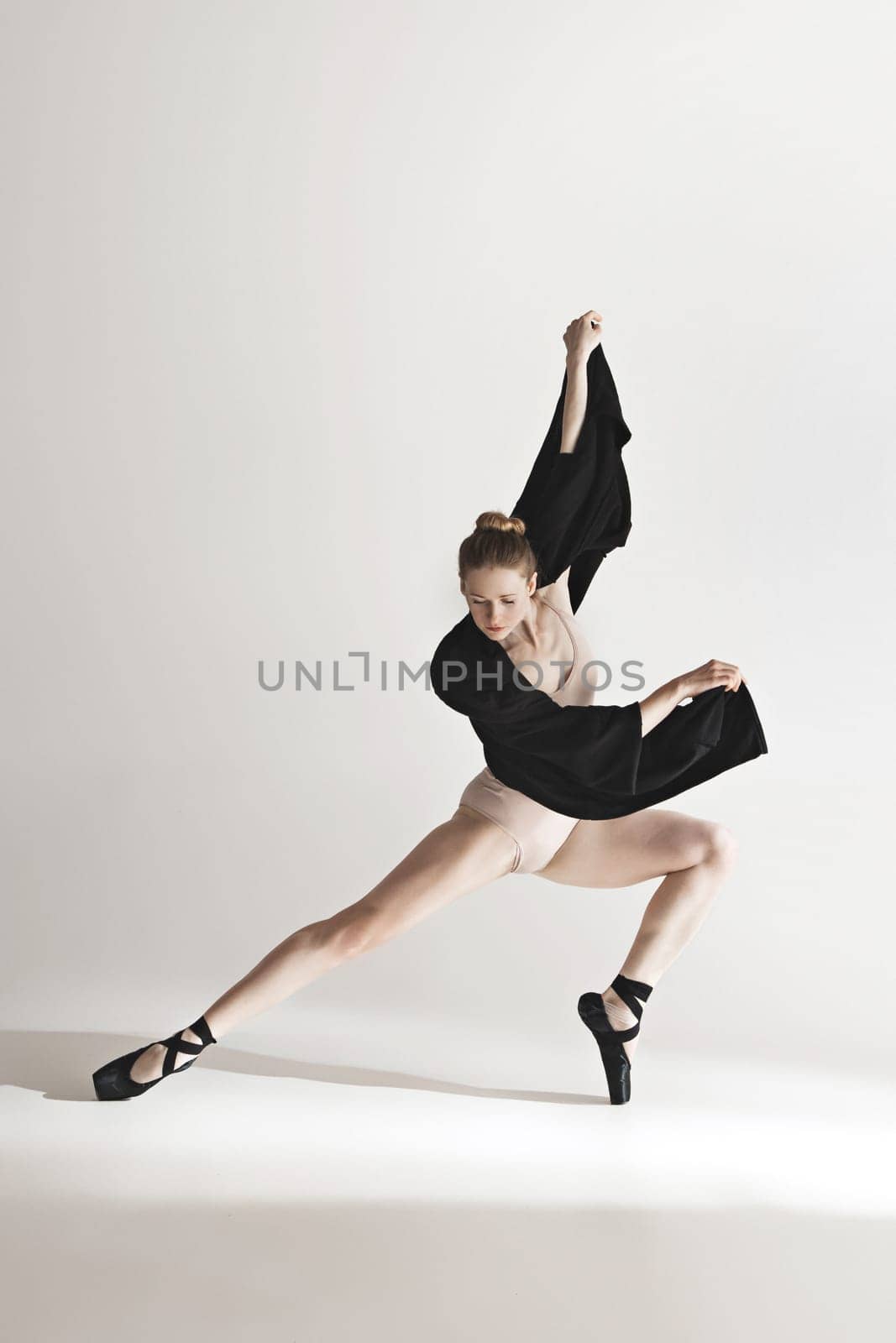 Young beautiful dancer in beige swimsuit dancing on gray studio background. Front view. Young female classical ballet dancer. Ballerina project. Modern choreography, contemporary. Fit caucasian moman