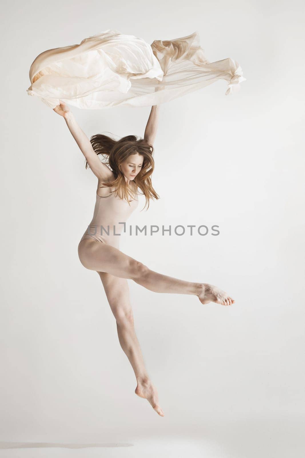 Young beautiful dancer in beige swimsuit dancing on gray studio background. Front view. Young female classical ballet dancer. Ballerina project. Modern choreography, contemporary. Fit caucasian moman