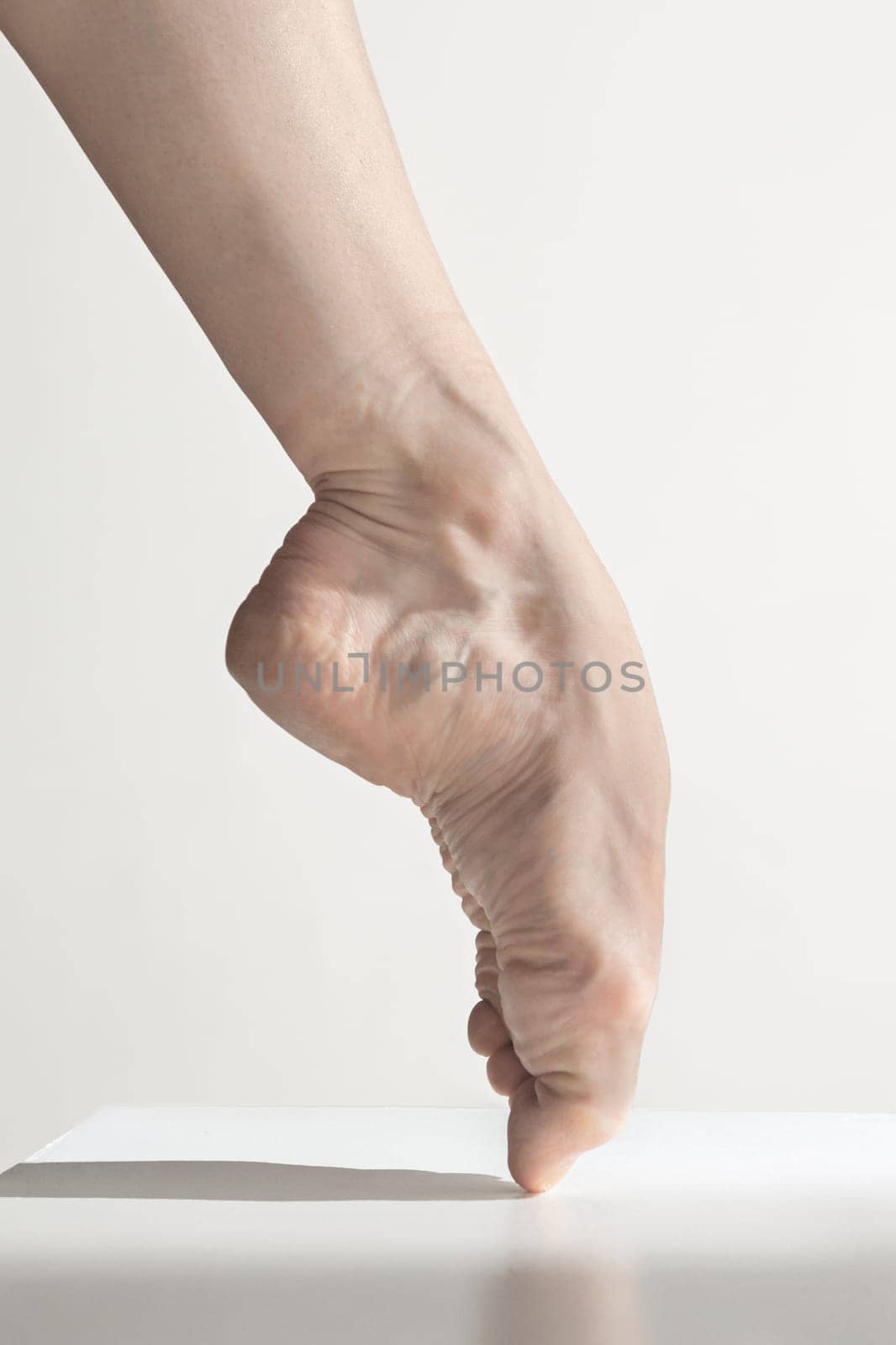 Close-up classic ballerina's legs on the white floor. Young female classical ballet dancer. Ballerina project. Modern choreography, contemporary. Fit caucasian moman. bare feet