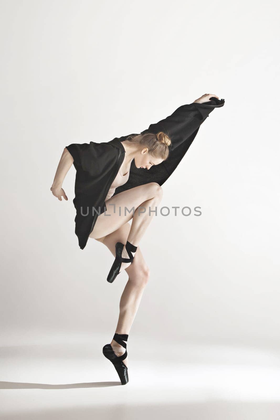 Young beautiful dancer in beige swimsuit dancing on gray studio background. Front view. Young female classical ballet dancer. Ballerina project. Modern choreography, contemporary. Fit caucasian moman