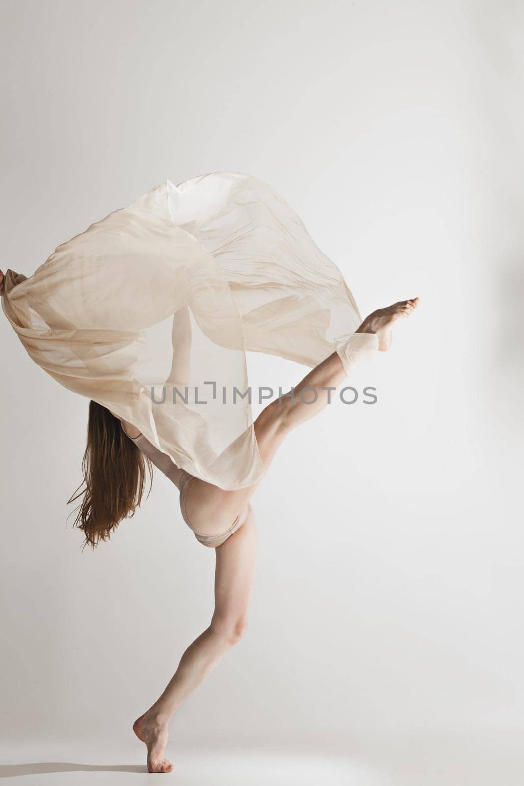 Young beautiful dancer in beige swimsuit dancing on gray studio background. Front view. Young female classical ballet dancer. Ballerina project. Modern choreography, contemporary. Fit caucasian moman