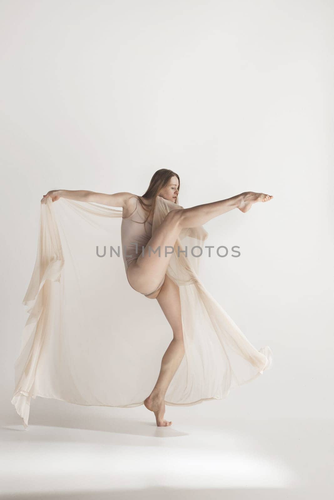 Young beautiful dancer in beige swimsuit dancing on gray studio background. Front view. Young female classical ballet dancer. Ballerina project. Modern choreography, contemporary. Fit caucasian moman
