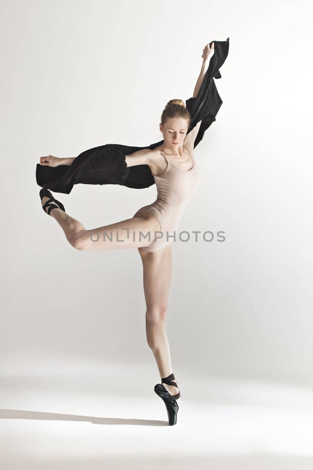 Young beautiful dancer in beige swimsuit dancing on gray studio background. Front view. Young female classical ballet dancer. Ballerina project. Modern choreography, contemporary. Fit caucasian moman