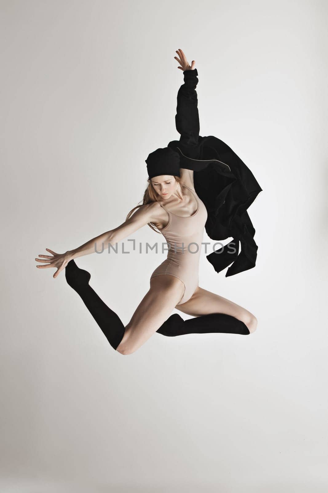 Young beautiful dancer in beige swimsuit dancing on gray studio background. Front view. Young female classical ballet dancer. Ballerina project. Modern choreography, contemporary. Fit caucasian moman
